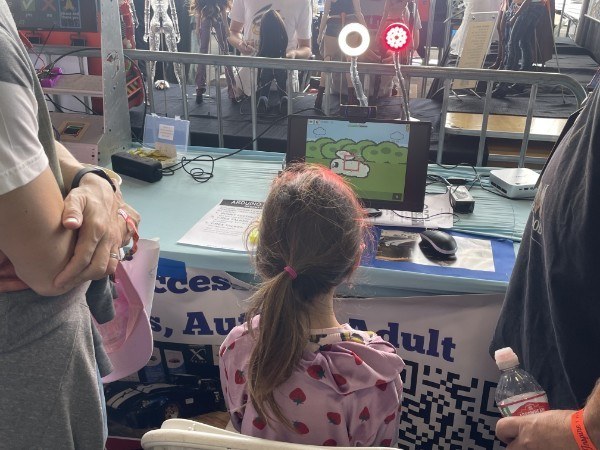 A girl in a polka-dot shirt, seen from behind, playing Bunny Feeding Frenzy with her eyes at the R.O.A.R. eye-tracking station at Maker Faire