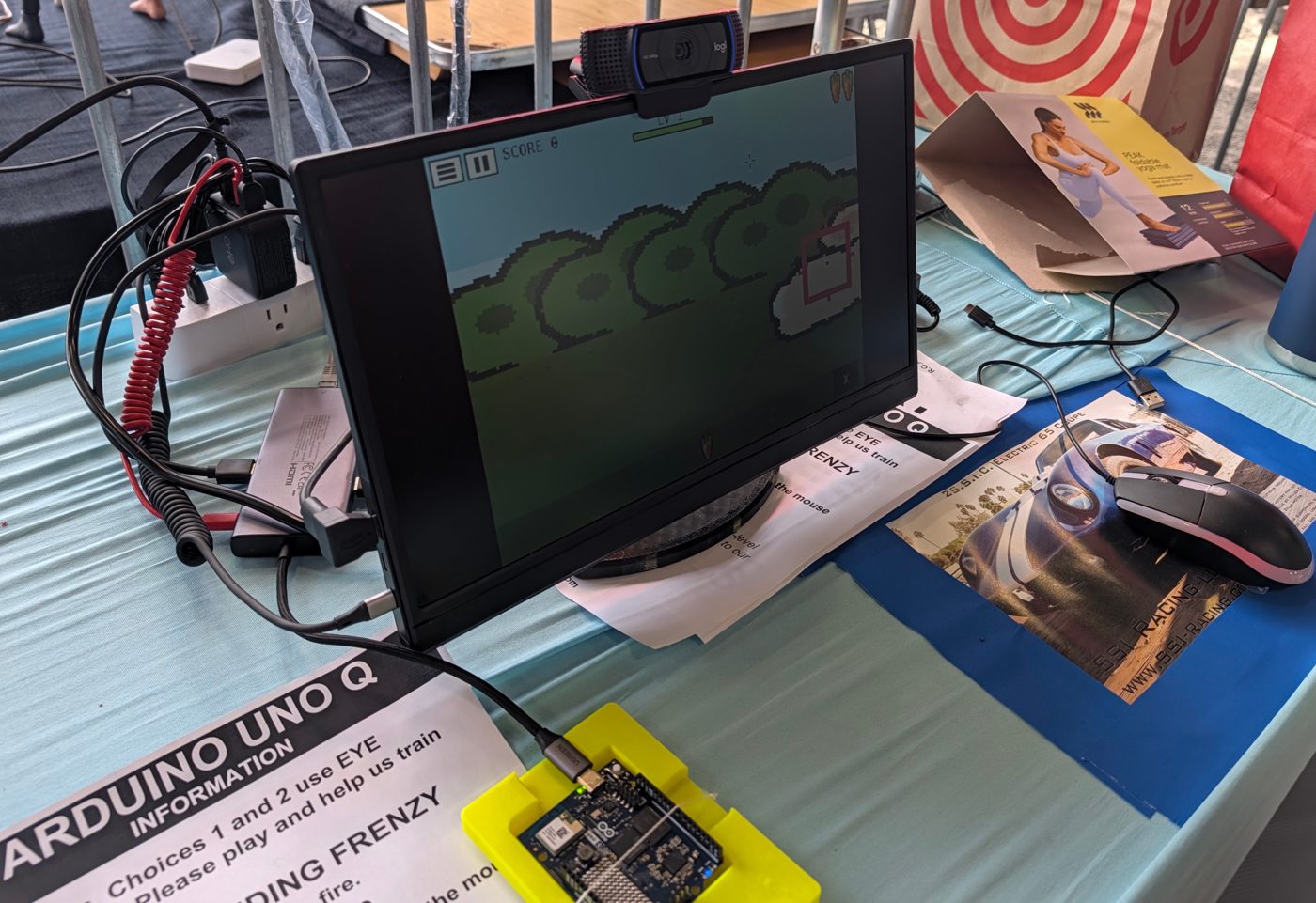The R.O.A.R. eye-tracking station at Bay Area Maker Faire 2026: Bunny Feeding Frenzy on a 15-inch screen, a webcam on top, and an Arduino UNO Q in a yellow 3D-printed case