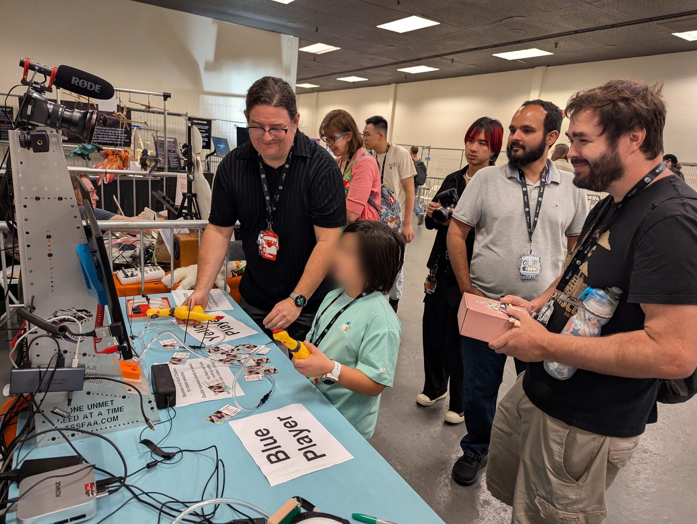 R.O.A.R. Rubber Chicken Challenge booth in action — a young visitor squeezing a yellow rubber chicken to play the game while T-Rex and other attendees watch
