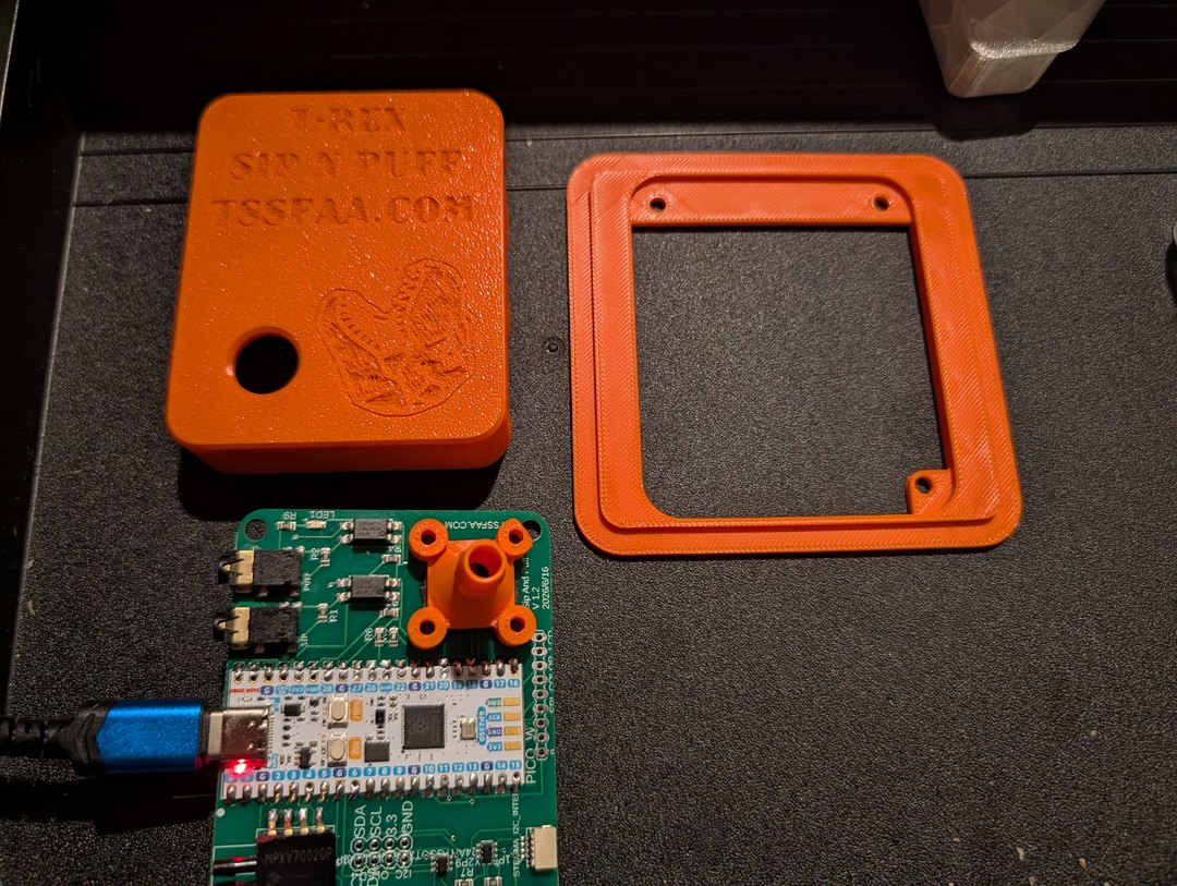 Sip-N-Puff V1.2 board next to its orange 3D-printed enclosure with T-Rex + chicken
